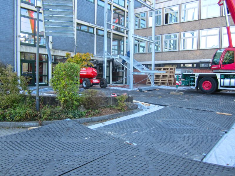 Ausgelegte Schwerlastplatten bilden sichere Arbeitsfläche für Mobilkran und Montagearbeiten am Schulgebäude.
