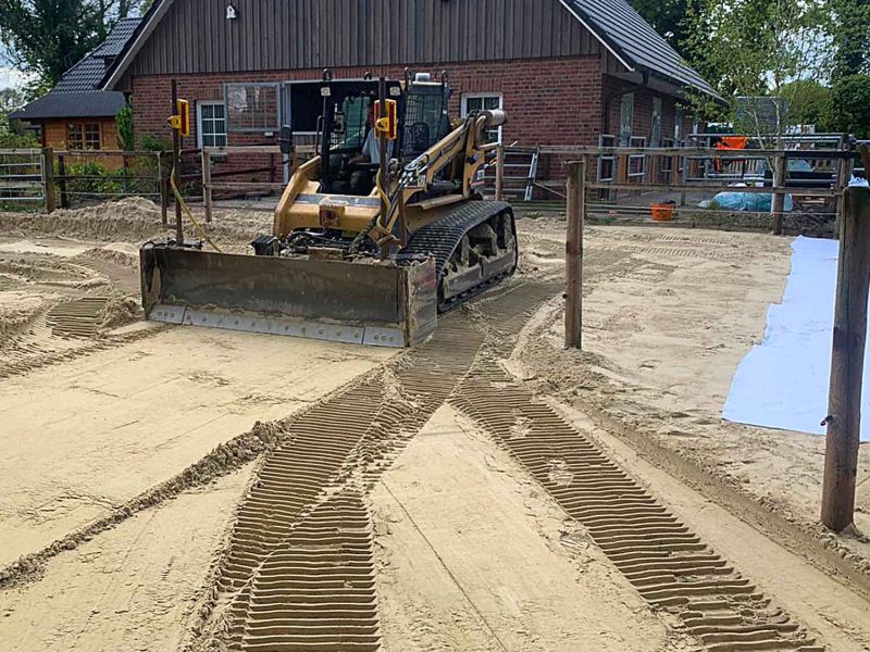 Ein Bagger verteilt Sand auf dem Boden als Grundlage für Bodenplatten