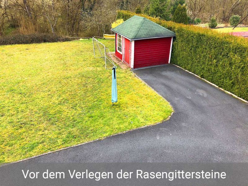 Eine Rasenfläche mit Fußballtor bei einer Hofeinfahrt. Ein Gartenhäuschen steht vor einer Hecke. Im Hintergrund ist ein Wald.