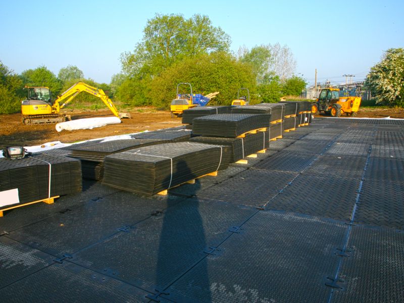 Gestapelte Platten auf Paletten mit Baufahrzeugen und Baumaschinen im Hintergrund.