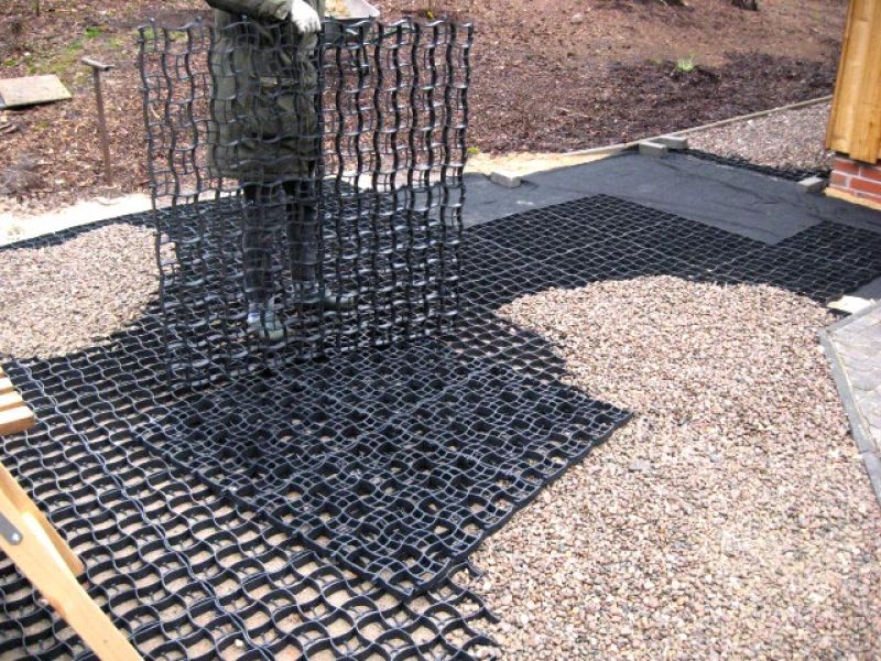 Ein Arbeiter verlegt ein schwarzes Bodengitter, das für die Stabilisierung einer Kiesfläche sorgt.