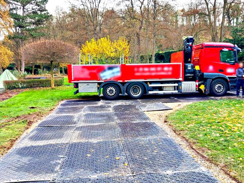 Ein roter LKW rangiert auf einer mobilen Baustraße aus Fahrplatten