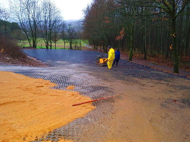 Arbeiter rütteln verlegte Paddockplatten mit einer Rüttelplatte in den feuchten Boden ein.