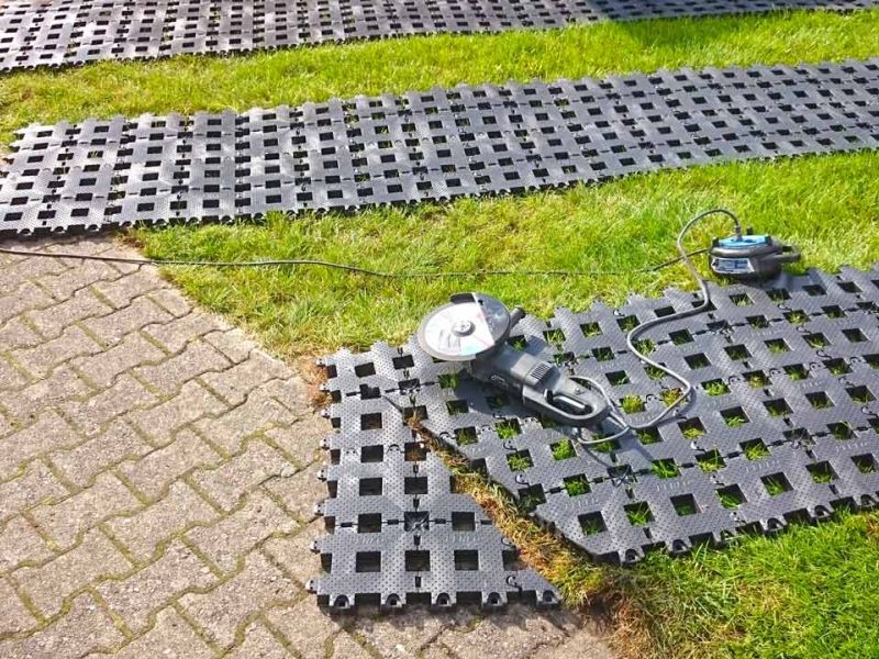 Kunststoff-Rasengitter wird mit einer Handkreissäge bearbeitet. Kabel und Werkzeug liegen auf dem Rasen.