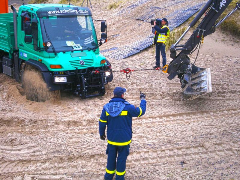 Bagger hilft beim Bergen eines Lkw aus tiefem Sand.