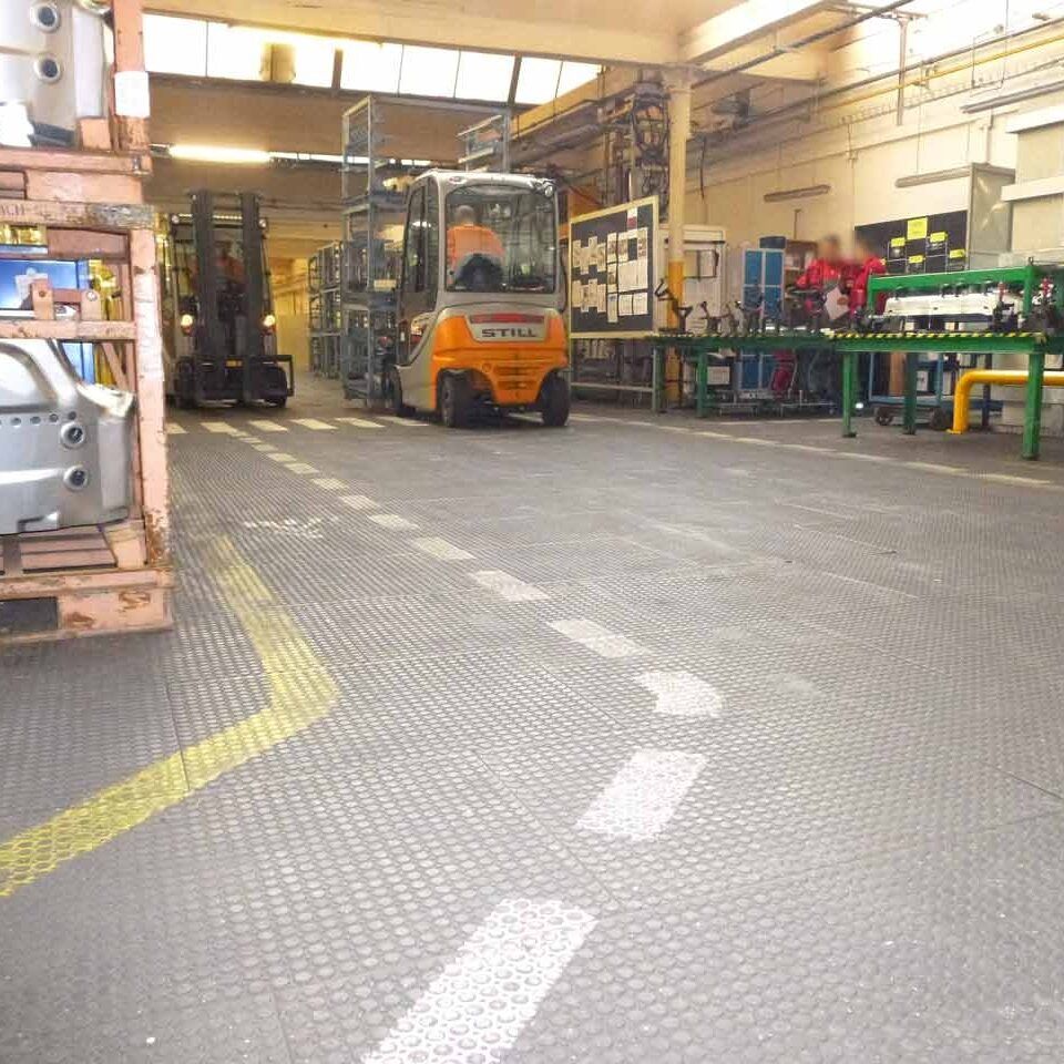 Ein Hallenboden ist mit Bodenmatten abgedeckt. Darauf fahren Gabelstapler.
