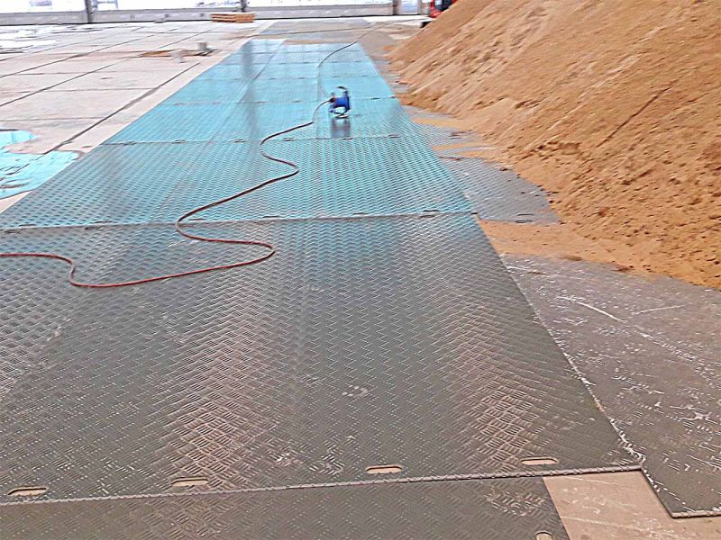 Verlegte Fahrplatten zum Betonschutz. Darauf ist ein Haufen Sand gelagert.