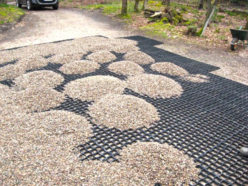 Mehrere Haufen Kies liegen auf einem Bodengitter bereit zur Verteilung für eine gleichmäßige Kiesstabilisierung.