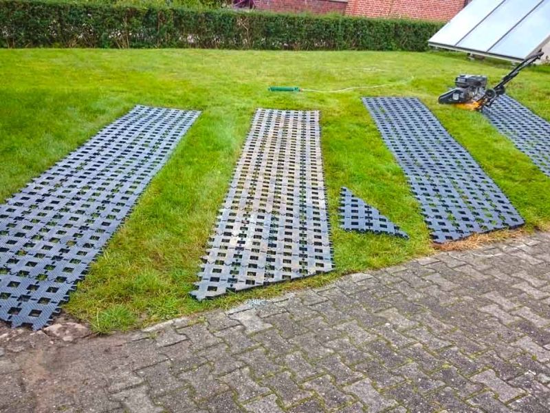 Kunststoff-Rasengittersteine auf Rasen mit zugeschnittenen Ecken. Eine Solaranlage und ein Werkzeug sind zu sehen.