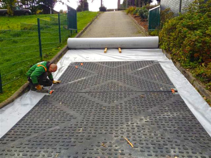 Arbeiter verlegt Kunststoffplatten auf Geotextil, um eine steile Zufahrt als stabile Kranstellfläche vorzubereiten.