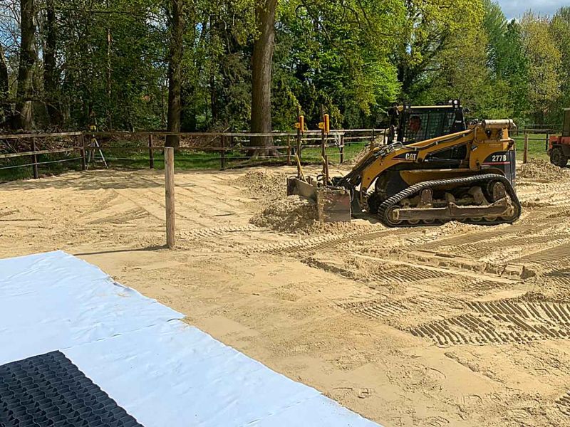 Ein Bagger begradigt eine Fläche aus Sand, damit darauf Bodengitter verlegt werden können