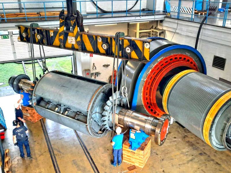 Ein Kranarm in einer Halle hebt die Spule eines Generators bei der Wartung an