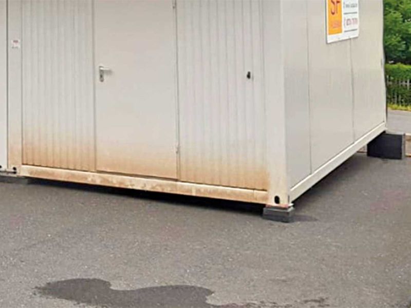 Ein auf Unterlegsteinen abgestützter Container auf einer Asphaltfläche mit Neigung