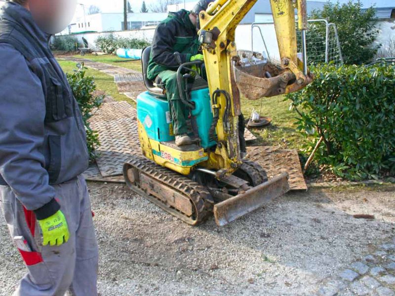 Ein kleiner Bagger fährt über Bodenschutzplatten, um den Untergrund bei Erdarbeiten zu schonen.