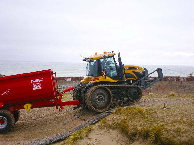 Raupentraktor fährt über sandigen Hang mit Bodenschutzplatten.
