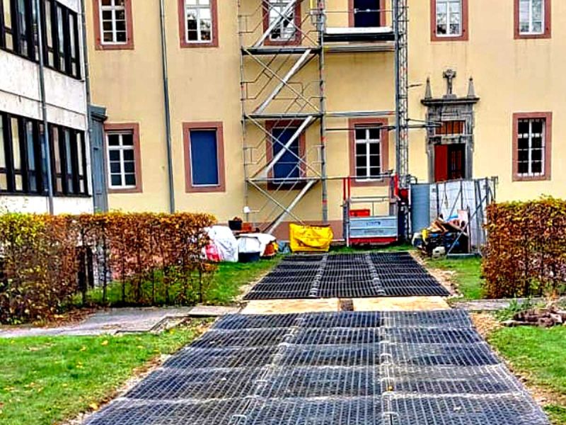 Vor einem großen Gebäude steht ein hohes Gerüst. Fahrplatten liegen auf dem Boden.