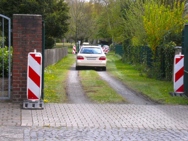 Auto fährt über schmale temporäre Zufahrt zwischen Gärten und Leitbaken.