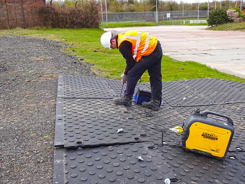 Ein Bauarbeiter verlegt die MaxiTrack-Schwerlastfahrplatte auf einer Wiese und Kiesuntergrund