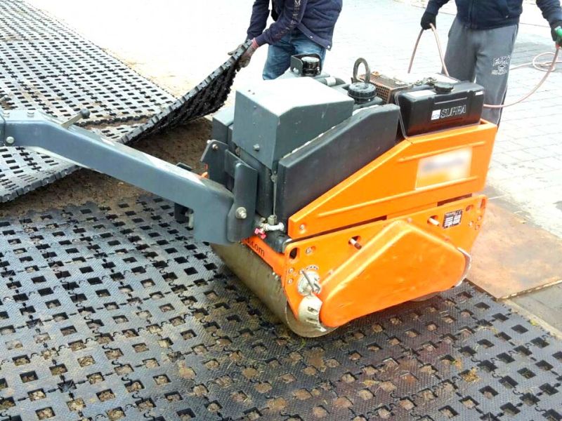 Eine kleine, orange Walze steht auf Kunststoff-Rasengittersteinen RGS35. Die werden so in den Erdboden eingedrückt.