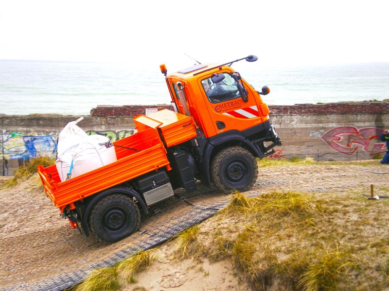 Multicar fährt über sandige Steigung mit Unterstützung durch Bodenschutz.