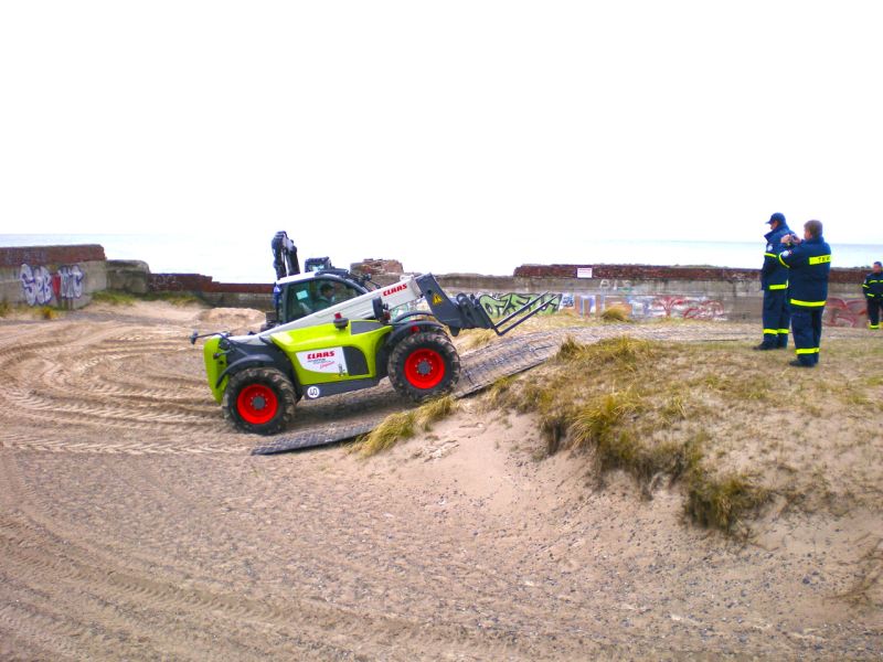 Kompaktlader überquert mit Bodenschutzplatten eine Sandkuppe.