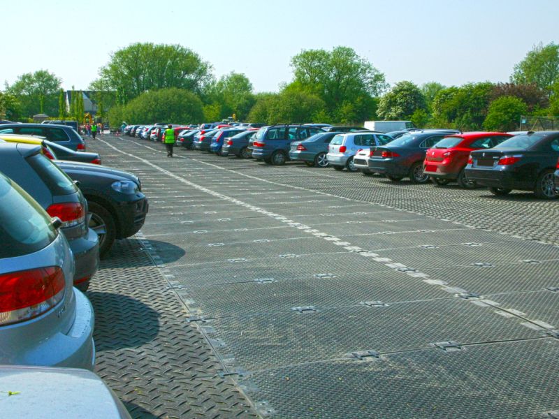 Parkende Autos auf befestigter Fläche mit Plattensystem in grüner Umgebung.