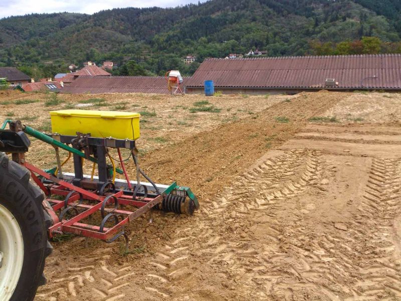 Ein Traktor glättet den Erdboden. Die Maschine hat eine gelbe Saatbox und mehrere Metallzinken, die den Boden auflockern.