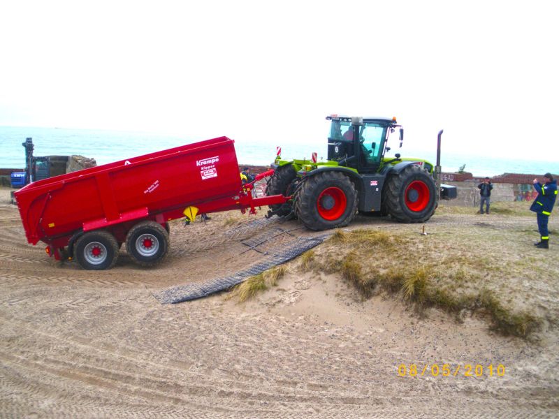 Traktor mit Anhänger fährt dank Platten über sandigen Hang.
