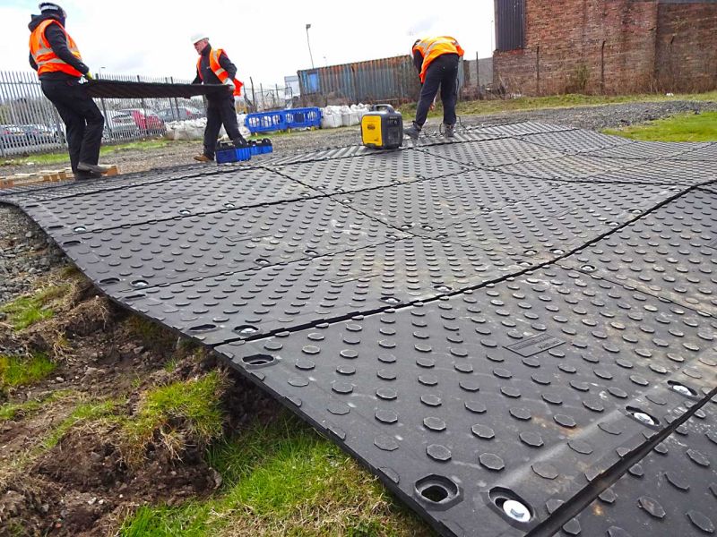 Bauarbeiter verlegen Kunststoff-Fahrplatten, um eine mobile Baustraße zu schaffen