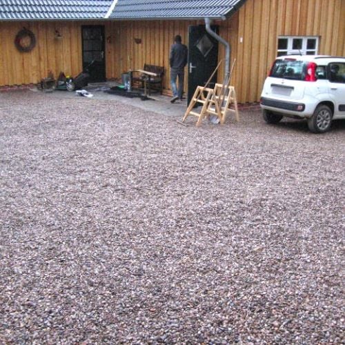Große Kiesfläche vor einem Holzhaus, bereits mit Bodengittern stabilisiert und vollständig aufgefüllt.