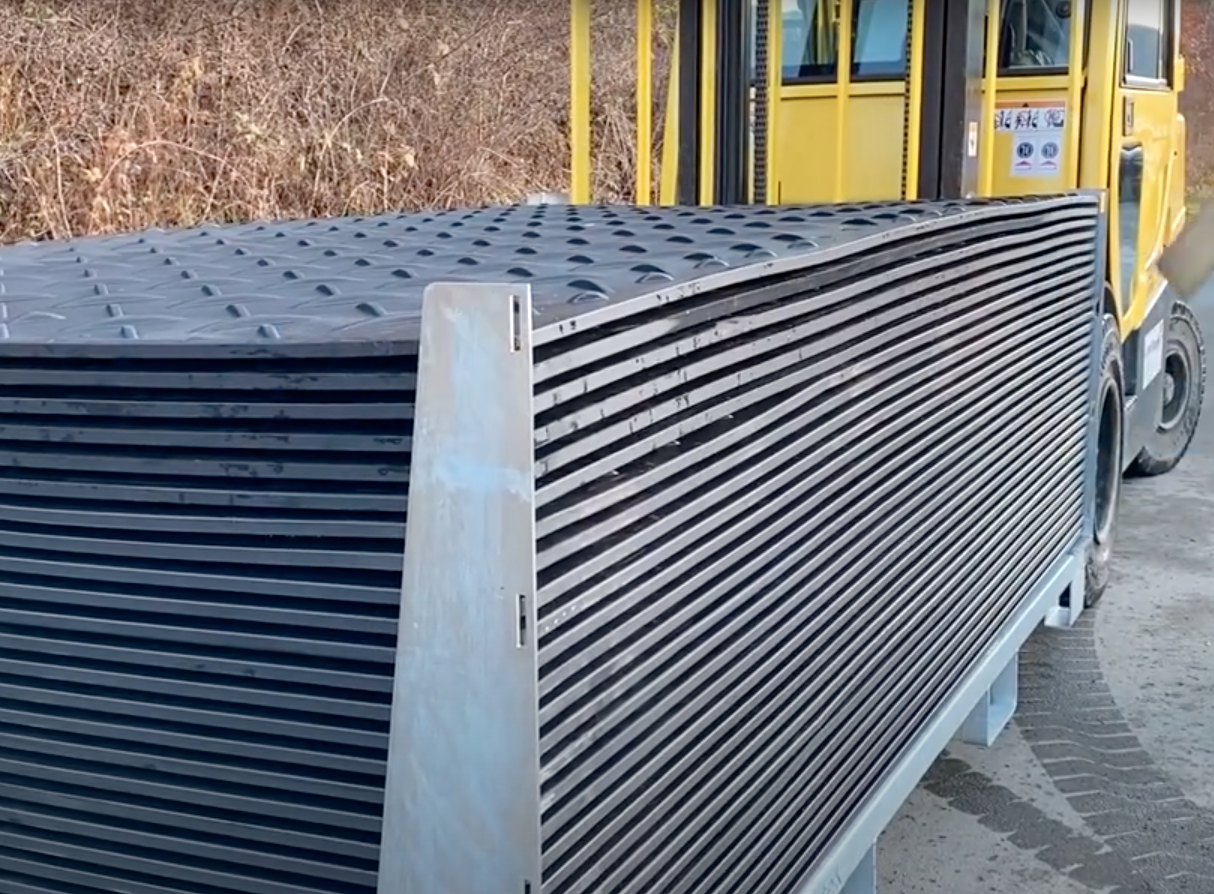 Transportgestell mit gestapelten Kunststoffplatten auf einer Baustelle neben einem Gabelstapler
