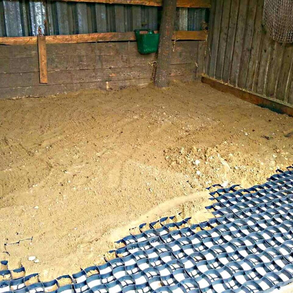 In einem Holzunterstand wurden Bodengitter verlegt. Darauf wird Sand verteilt, der die Gitter teilweise bedeckt.