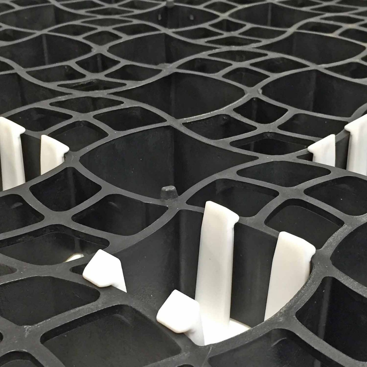 Nahaufnahme einer schwarzen Kunststoff-Wabenplatte mit weißen Verstärkungselementen zur Stabilisierung von befahrbaren Flächen.