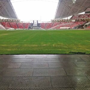 Blick auf den Rasen einen Stadions. Am Rand sind Bodenmatten verlegt. Im Hinergrund sieht man die Tribünen.