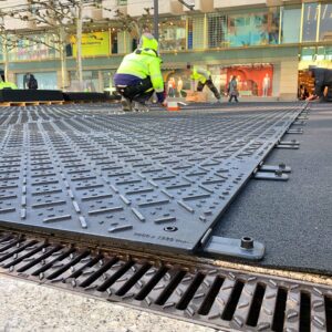 Arbeiter verlegen Bodenschutzplatten auf Asphaltfläche im Stadtgebiet für temporäre Wege oder Schutzflächen.