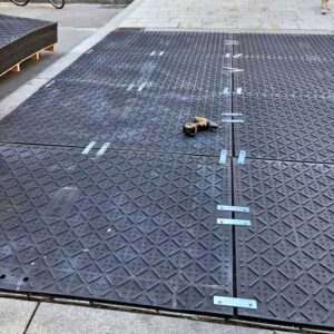 Bodenschutzplatten mit blauen Metallverbindern fest verschraubt – stabile Fläche auf Baustelle.