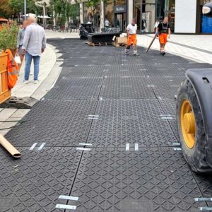 Arbeiter verlegen Bodenschutzplatten in der Stadt, um eine sichere Fahrbahn und Schutzfläche zu schaffen.