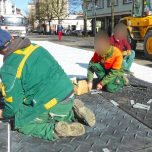 Arbeiter befestigen Bodenschutzplatten mit Verbindungsstücken auf einer Baustelle im städtischen Bereich.