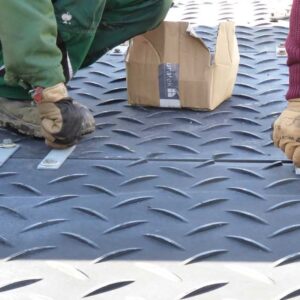 Arbeiter montieren Bodenschutzplatten mit Stahlverbindern auf strukturierter Oberfläche für sicheren Halt.