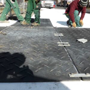 Arbeiter verbinden Bodenschutzplatten auf heller Fläche mit Metallverbindern für eine stabile Fahrbahn.