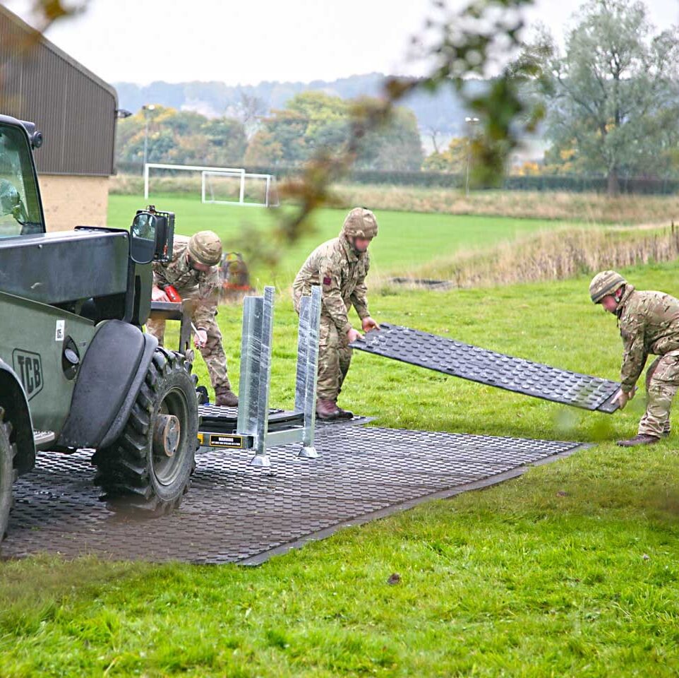 3 Männer in Militär-Uniform verlegen Schwerlastplatten auf einer Wiese.