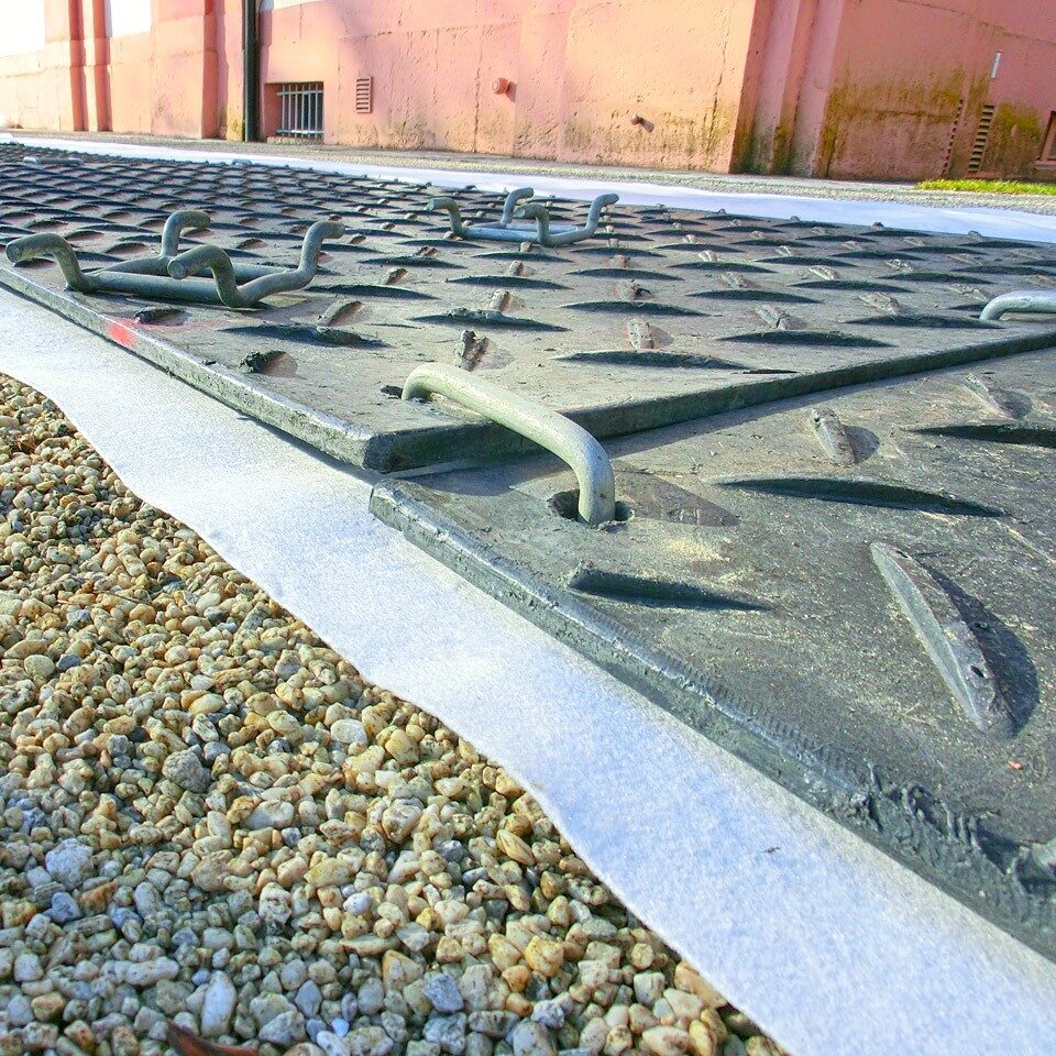 Bodenschutzplatten mit Verbindungsstiften auf Geotextil und Schotteruntergrund für stabile, saubere Arbeitsflächen.