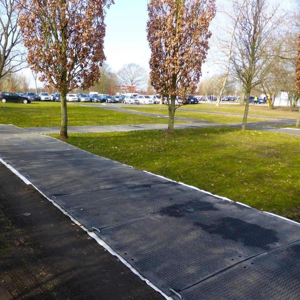 Verlegte Bodenschutzplatten schaffen einen festen, rasenschonenden Weg durch eine Park- und Wiesenfläche.