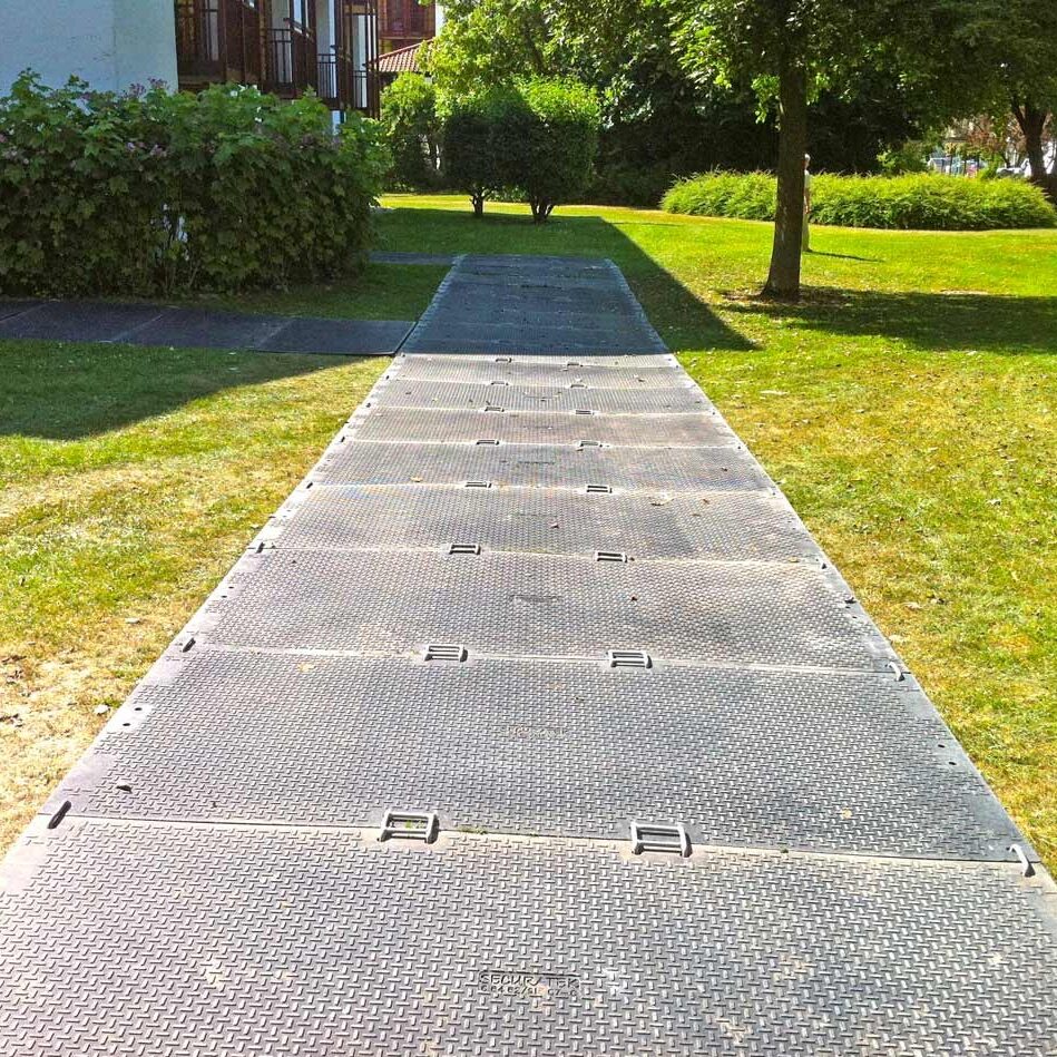 Verlegte Bodenschutzplatten bilden einen geraden, stabilen Weg über eine gepflegte Rasenfläche.