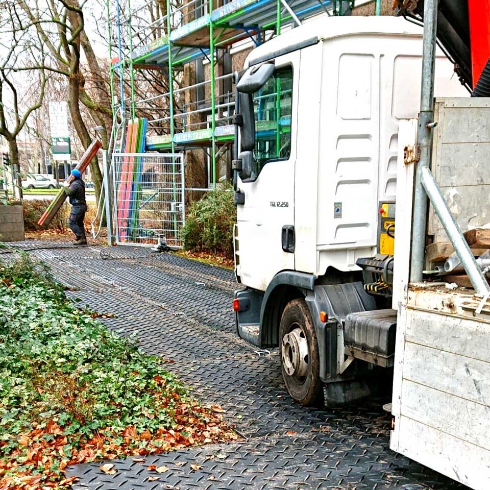 Ein Lkw fährt über Bodenschutzplatten, die eine sichere Zufahrt zur Baustelle über Rasen und Wege ermöglichen.