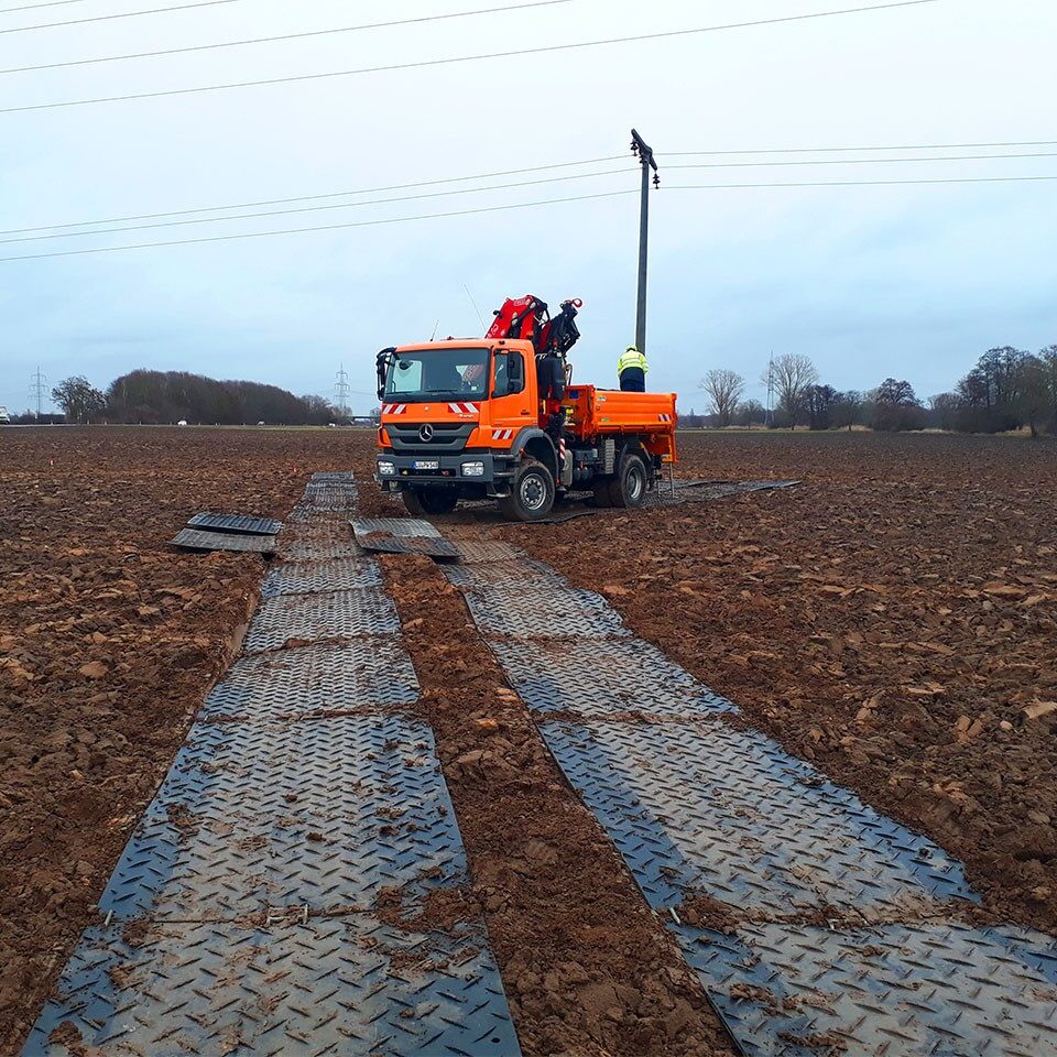 Ein Baustellenfahrzeug steht auf Bodenschutzplatten, die als Fahrstraße über einen Acker verlegt sind.