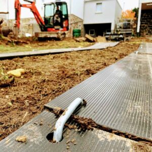v:tek Fahrplatten im Verbund verlegt auf einem erdigen Boden. Im Hintergrund steht ein Mini-Bagger.
