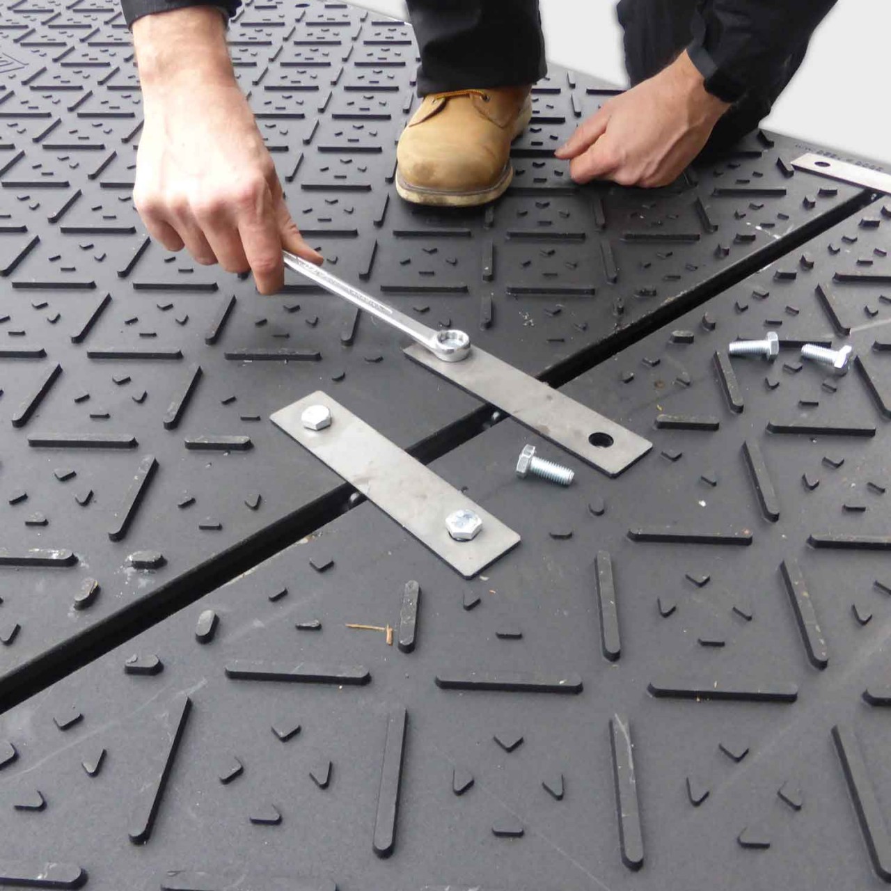 Arbeiter befestigen Bodenschutzplatten mit Stahlverbindern und Schrauben für eine stabile Verbindung.