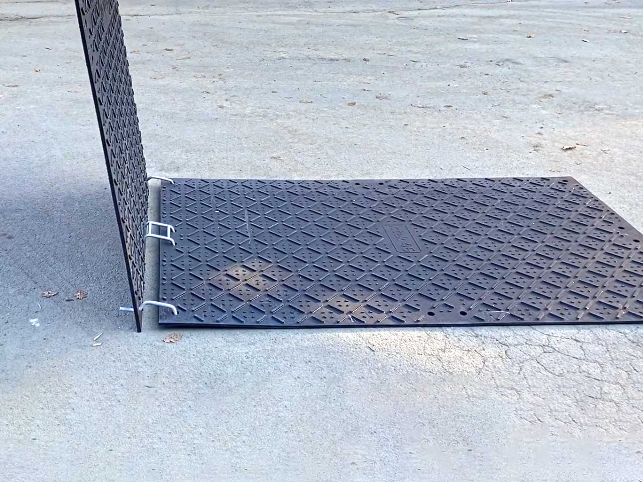 Auf einer Straße werden Bodenschutzplaten verlegt. Die Fahrplatten werden mit Verbindern aus Stahl verbunden.