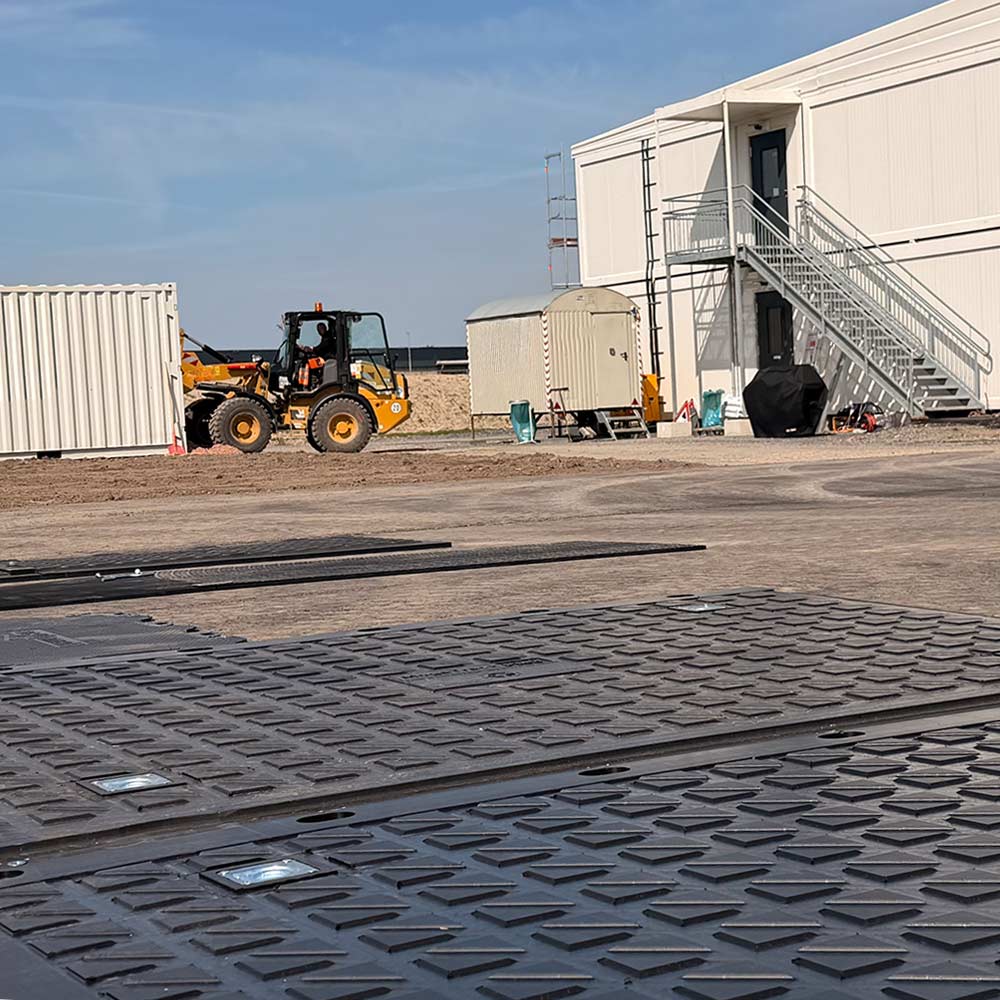 Befestigte Arbeitsfläche mit MegaTrack PRO Schwerlastplatte vor Containeranlage auf Baustelle für sicheren Maschinenverkehr